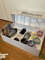 Box opened showing entire Magic Bullet blender set packed in white foam insert, including cups, blades, motor base, rings, and recipe manual.