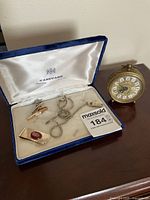 Small vintage style alarm clock and open case of men's accessories including money clip, tie clips, and watch chain
