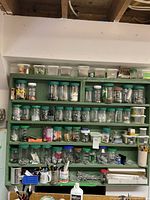 Full view of green wooden shelves with numerous jars and containers filled with various nails, screws, bolts, and other small hardware parts.