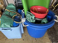 Multiple buckets including blue and gray buckets with white rope handles filled with tarps and ropes.