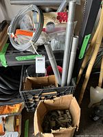 Photo showing coil of 11 gauge bottom wire, metal pipes in a plastic crate, and several containers with nails and small items on a shelf labeled 'chain link fence hardware'