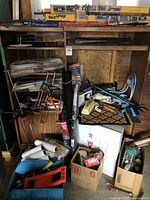 General view of the various painting and carrying tools, paint rollers, brushes, panel carrier, shelf brackets, caulking supplies, and miscellaneous boxes and hardware organized on a wooden shelving unit.