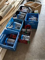 Multiple plastic crates on floor each filled with various jars and containers holding screws, nails, bolts, and nuts