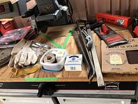 Overview of mixed tools and accessories including gloves, safety glasses, tape roll, and saw blades on a wooden surface.