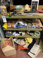 Photo showing 3-tier green metal shelving unit with multiple paint tools including rollers, brushes, scrapers, tape, gloves, and a caulking gun.