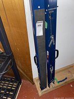 Pair of blue metal folding saw horses standing upright, compactly folded, against a wooden surface.