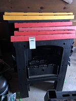 Stacked view of four black folding sawhorses with two yellow and two red rulers on top, showing rulers and upper structure