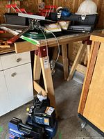 Pair of wooden sawhorses shown in a workshop setting with other tools around.