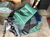 Multiple tarps folded and stacked, colors green, gray, blue, and black visible.