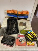 Overview of two hex key sets, staple gun, black tray with hex keys and wrenches, boxes of staples, small metal tin, bolts, and other tools.