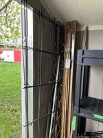 Wide angle photo showing bamboo stakes and black metal trellises leaning against the wall in a shed.