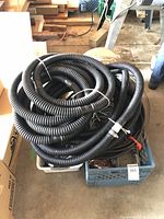 Coiled thick black flexible corrugated tubing in a blue crate, showing multiple coils and connectors on cables.