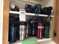 Photo of assorted water bottles and travel coffee cups in a cabinet, showing stainless steel and plastic varieties with visible brand labels like Tim Hortons and Costco.