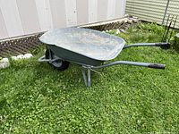 Side angled view of the wheelbarrow on grass showing metal tub, handles, and wheel.