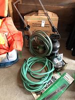Wide view of the lot showing wood and masonry sprayer, coiled green garden hoses, box of landscape edging, and other smaller items.