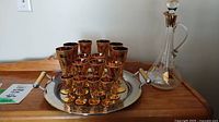 Photo showing six amber and gold champagne flutes, five wine glasses, four aperitif glasses on a metal tray with wicker-wrapped handles