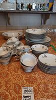 Full set arranged on table showing multiple place settings including plates, bowls, cups, saucers, creamer, sugar bowl, and serving platter.