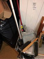 Cleaning tools including metal dustpans and brooms with wooden handles, showing age and use.
