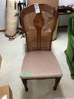 Full view of the wooden dining chair showing cane backrest and upholstered seat, positioned in a basement setting.