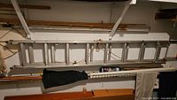 Side view of the 10-foot aluminum extension ladder hung on a wall rack alongside other items in a garage. Shows rope tied on the ladder frame.