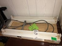 Two white metal grow light fixtures laid on a wooden surface with a cord coiled on top. Fixtures show signs of dirt and wear.