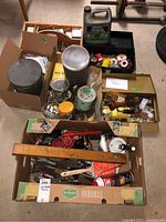 Box containing hardware and tools including paint cans, wooden level, hand drill, hammers, screwdrivers, clamps
