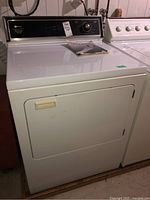 Front and top view of the Maytag dryer showing control panel, door, and user manual on top