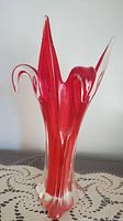 Red art glass vase with clear edges and abstract sculptural design shown upright on lace tablecloth.
