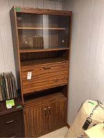 Full front view of tall MDF hutch showing glass sliding door, drop-front drawer, open shelf, and double door cabinet at bottom with brass handles.