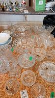 Wide view of multiple crystal glassware pieces on a patterned tablecloth showing a variety of items like decanter, bowls, and glasses.