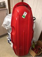 Photo showing the bottom side of one red plastic toboggan with visible wear and black pull rope tied at the front.