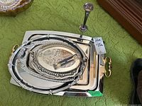 Photo showing stacked silverplate serving trays with gold-toned handles and small metal vase in background