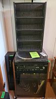 Full stereo system stacked in wooden cabinet with glass door and wheels. CD rack is on top. Cabinet dimensions tag visible.