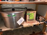Aluminum pot with lid and metal strainer boxed next to it on a shelf.