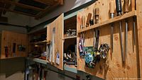 Wide view of storage cabinets and pegboard with various hand tools and accessories including saws, screwdrivers, files, key chains, spools.