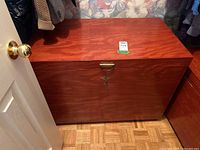 Front angle showing the wooden trunk with brass handle and key lock with smooth reddish-brown polished finish.