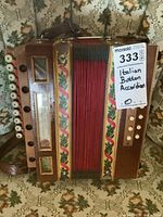 Front view of accordion showing wooden body, red bellows, decorative painted borders, and sale tag