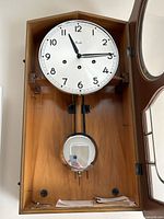 Wall clock in open walnut veneer case showing dial, pendulum and interior