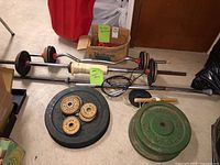 Overview of the weight lifting equipment including barbells with weight plates, dumbbells, and additional small weights with rope and accessories