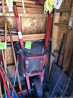 Wheelbarrow with red metal frame, metal tray, and a single large black wheel in a barn environment, showing signs of usage and wear.