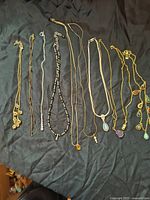 All 10 necklaces laid out flat on a black background, showing varied chain styles and pendants including colored jewel-like drops and beads.