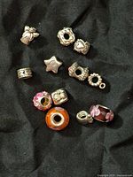 12 silver charm beads with various designs including hearts, stars and floral glass beads on a black background.