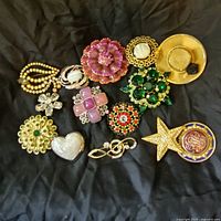 Full view of the 14 costume jewelry pins laid out showing various shapes and colors including pink flower, gold star, heart, hat, and green rhinestone floral clusters.