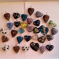 Overview photo showing 31 variously colored and patterned handblown glass heart pendants arranged on a light background.