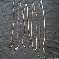 Five sterling silver necklaces laid out on black fabric, showing the varied styles and pendants on two pieces.