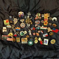 Full assortment of pins laid out against a black background showing a wide variety of designs, flags from different countries, Olympic, and promotional pins.