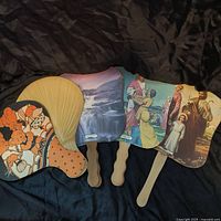 Five church hand fans showing various religious and scenic prints with wooden handles.