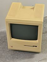Front view showing built-in CRT screen, floppy disk drive, and Apple rainbow logo.