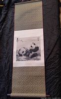 Shows full length of the silk wall hanging laid out flat on a black surface, highlighting the patterned silk borders and central panda artwork.
