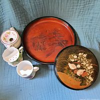 Overview of all five items together on blue fabric: two mustache cups, ladies spittoon, carved wooden bowl, and Otagiri box.